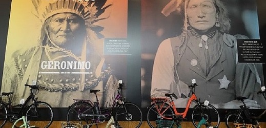 Zeď s plakáty indiánů nad vystavenými koly značky Apache.